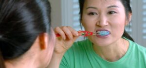 adult brushes her teeth while being sick with braces